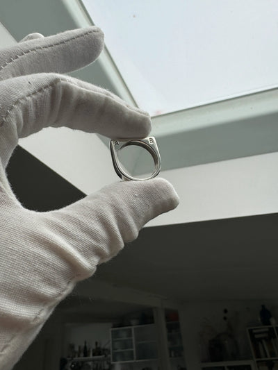 Ein schlichter, individuell gefertigter Ring mit einem gestempelten Buchstaben, der die handwerkliche Qualität von Zweisilber hervorhebt.
